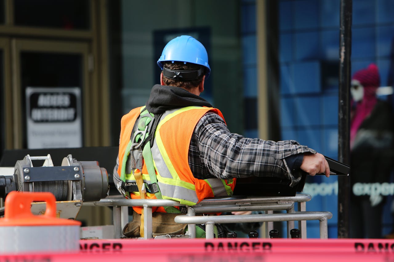 about-01 A construction worker wearing a blue helmet and safety vest operates equipment at an urban construction site.