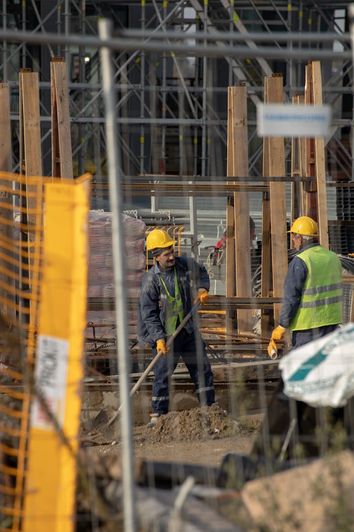 about-02 Construction workers in hard hats at an active building site with safety barriers.