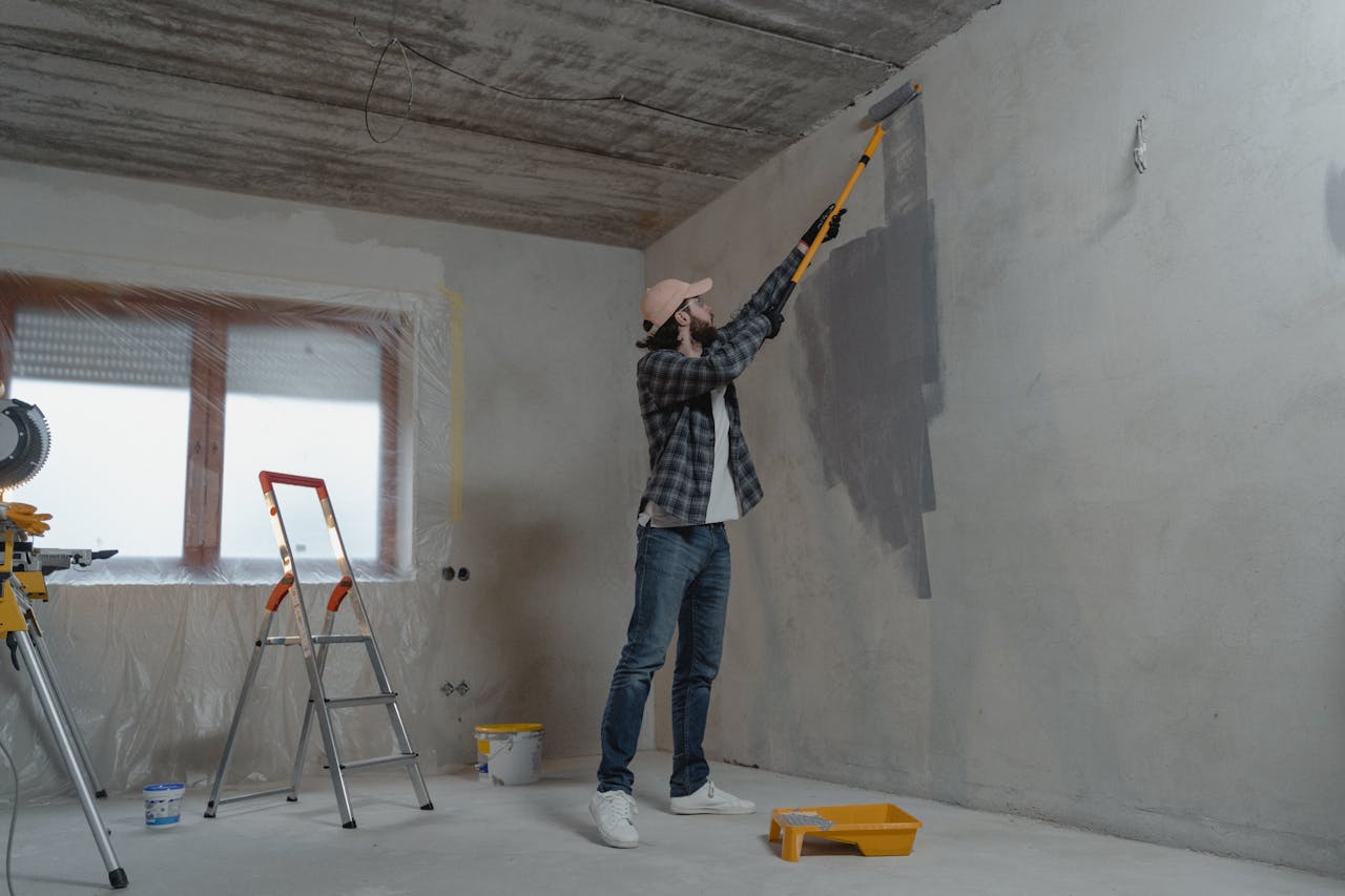 about-03 A man painting an interior wall with a roller during a home renovation project.
