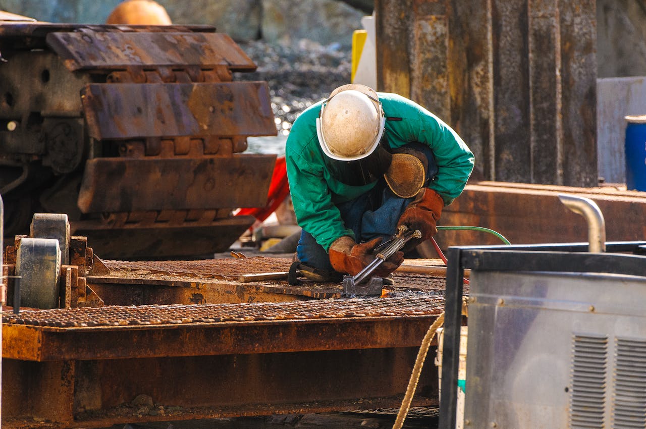 about-01 A welder in protective gear works at a construction site outdoors.