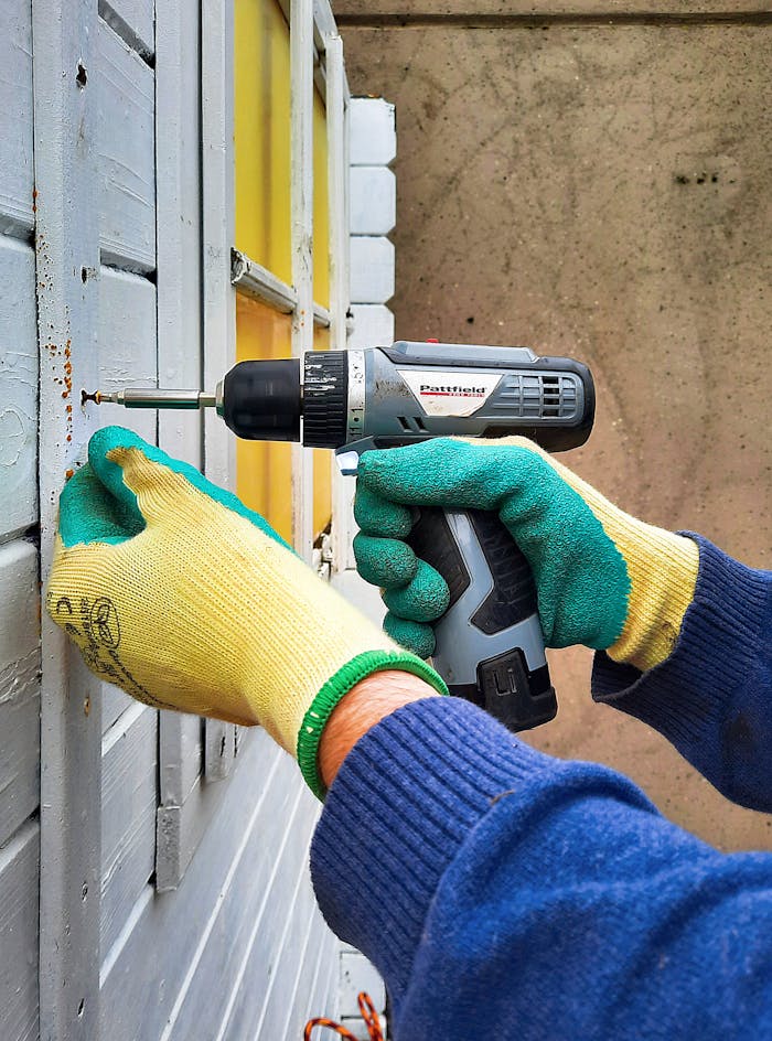 about-02 Close-up of a construction worker using a drill on a wooden wall, focusing on hands and tool.